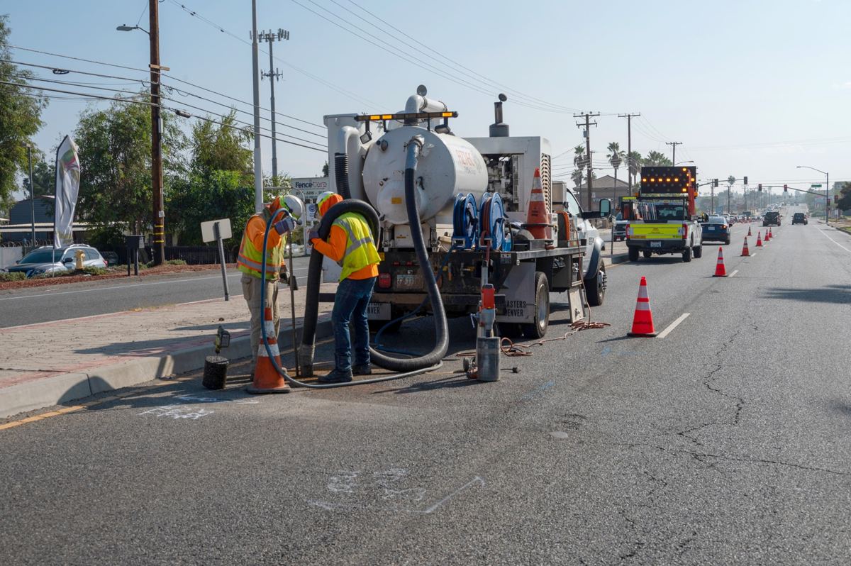 Crew using a hydrovac truck to pothole and expose a buried utility along a roadway